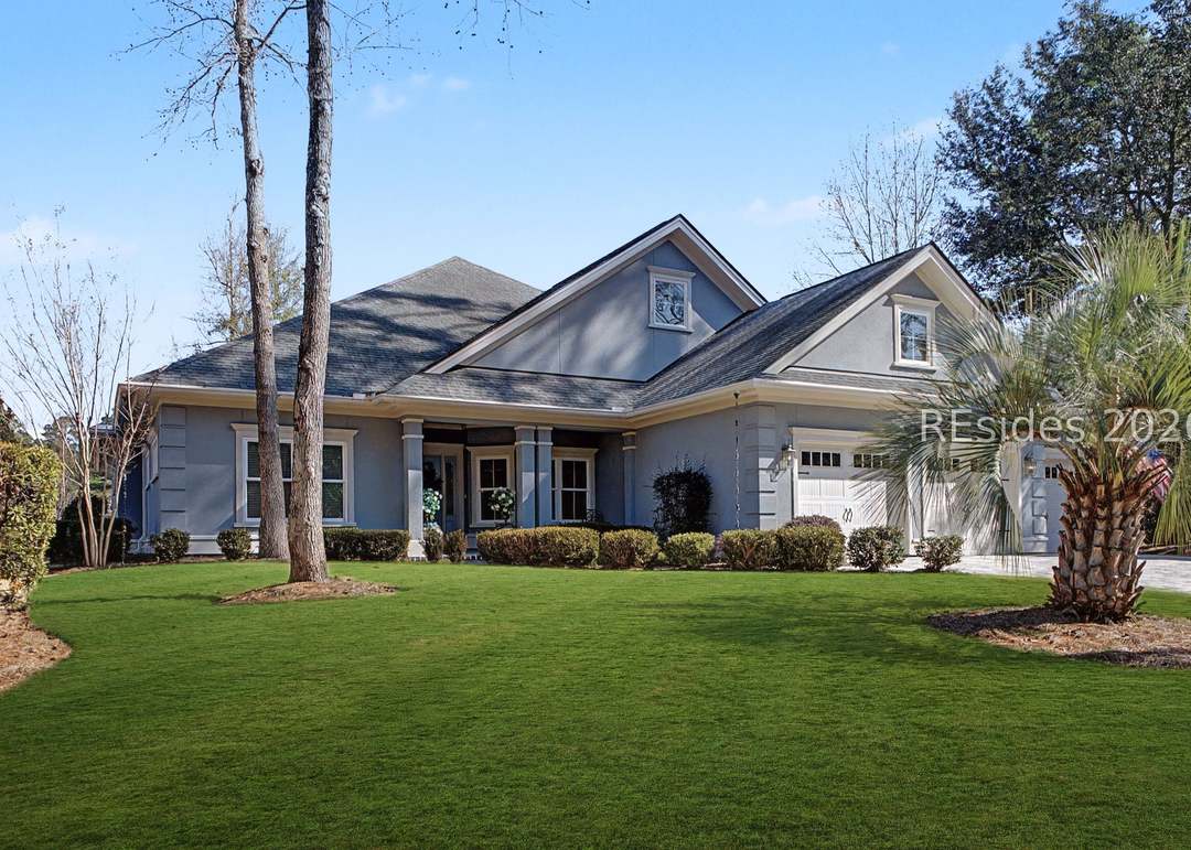 Full front elevation of the 2015 custom Lowcountry home, gray board-and-batten with white columns, palms flanking the entry and a single peaked roofline