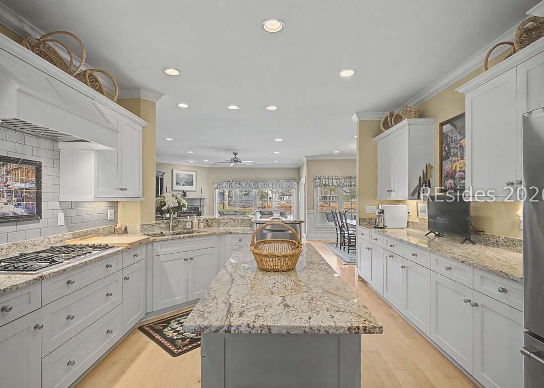 Custom kitchen with white shaker cabinetry, granite countertops, large center island, subway tile backsplash, stainless gas cooktop and view through to the breakfast room with lagoon-side windows beyond