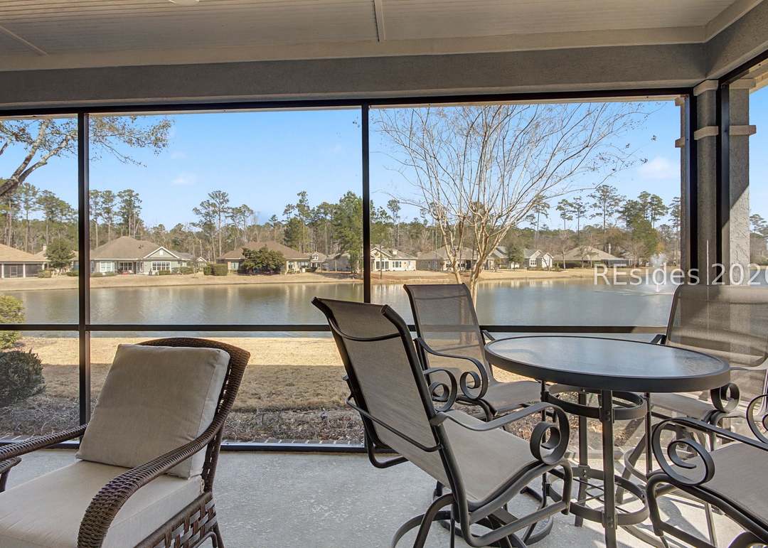 View from inside the screened lanai out over the lagoon, a row of homes visible across the water beneath bare winter trees and a clear Carolina blue sky