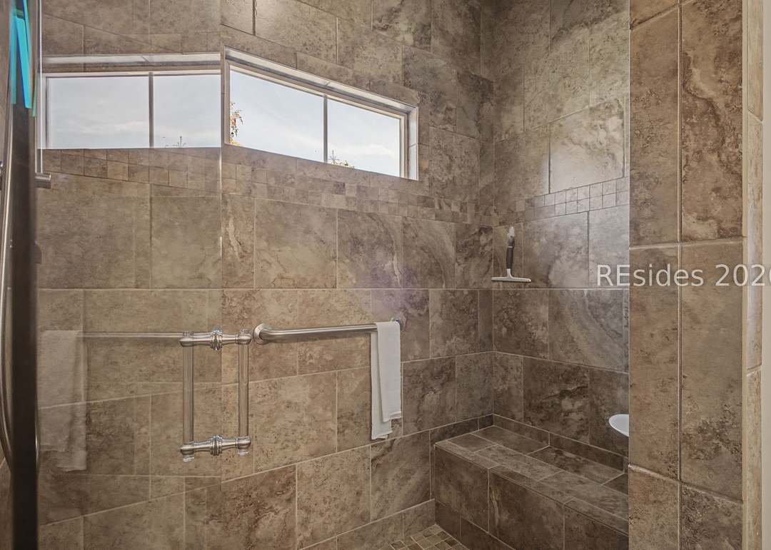 Walk-in tiled shower in the primary bath with a clerestory window, built-in bench seat, multi-zone showerheads and warm travertine-pattern tile
