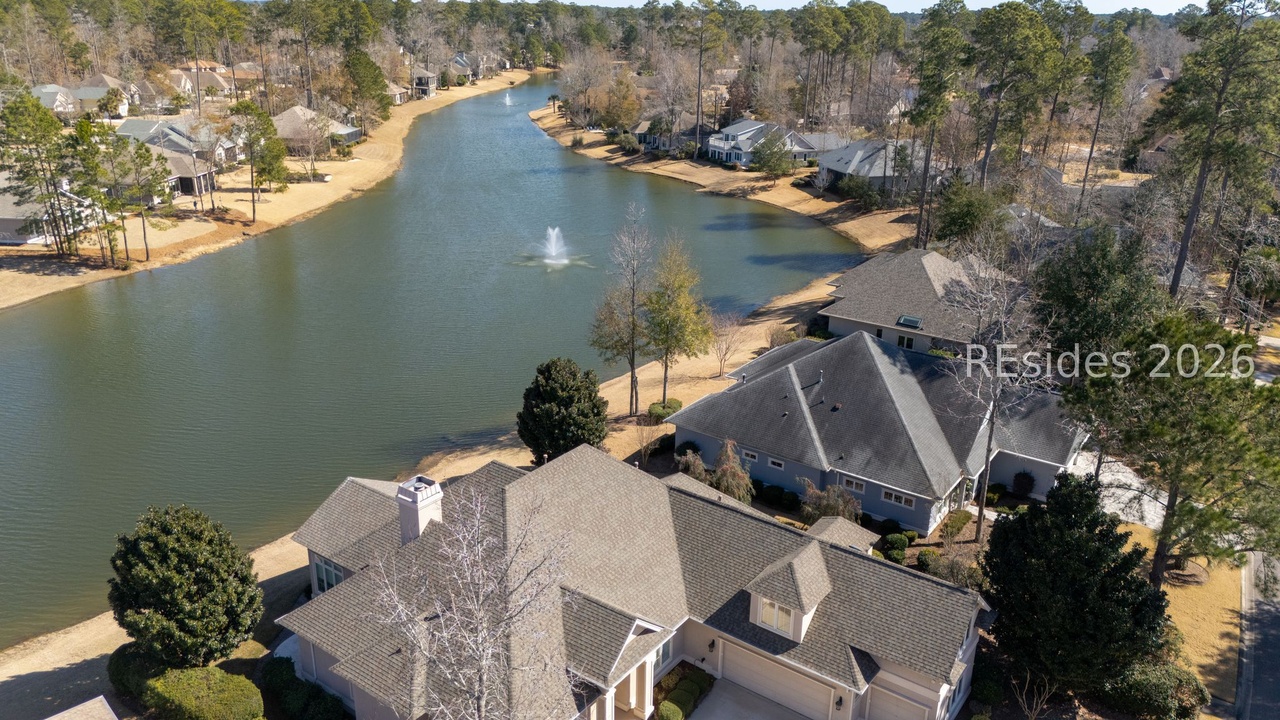 Aerial view of 40 Catamaran Ln framed by Lowcountry pines, with the home set at the curve of Riverbend's central lagoon and a fountain in the open water